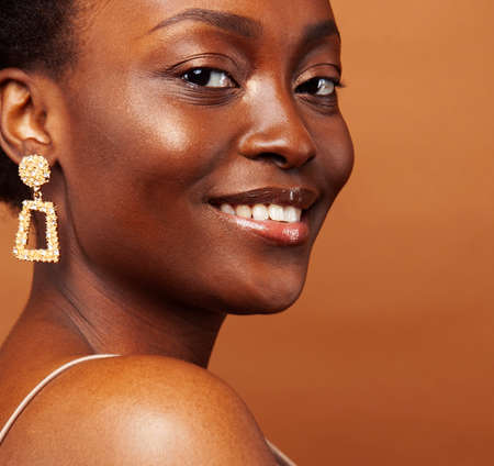 pretty young african american woman with curly hair posing cheerful gesturing on brown background,...