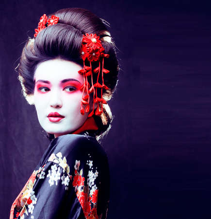 young pretty real geisha in kimono with sakura and decoration on black backgroundの写真素材