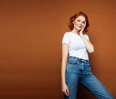 young pretty redhead girl posing cheerful on warm brown background, lifestyle people concept
