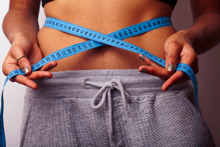 woman measuring waist with tape on knot, african tan isolatedの写真素材