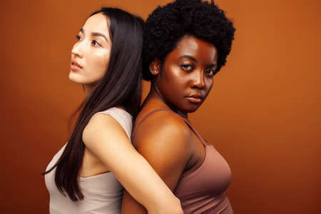young pretty asian, african american woman posing cheerful together on brown background, lifestyle diverse nationality people conceptの写真素材