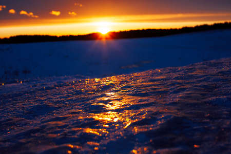 winter landscape: snow and ice in field, pink colorful sunset