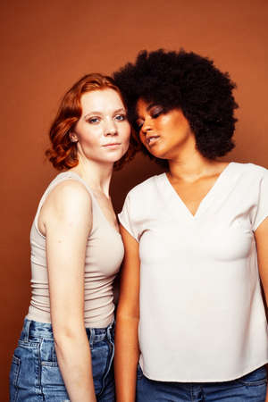 young pretty african and caucasian women posing cheerful together on brown background, lifestyle diverse nationality people conceptの写真素材