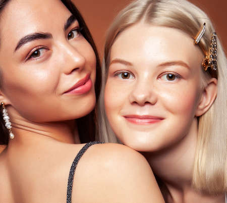 two pretty diverse girls happy posing together: blond and brunette, caucasian and asian on brown...