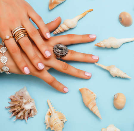 beautiful woman hands with pink manicure holding plate with pearls and sea shells, luxury jewelry...