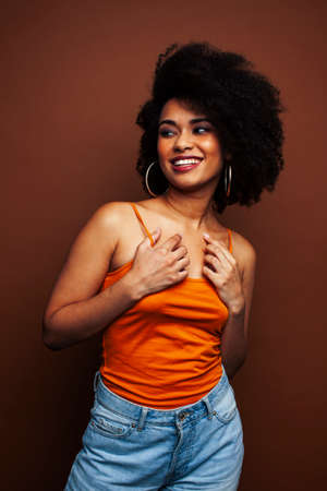 pretty young african american woman with curly hair posing cheerful gesturing on brown background,...