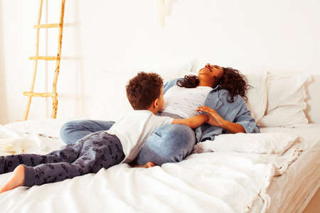 young pretty african american mother with son in bed at morning playing, happy family, lifestyle people conceptの写真素材