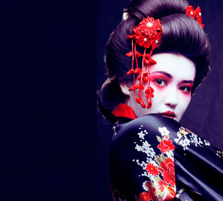 young pretty real geisha in kimono with sakura and decoration on black backgroundの写真素材