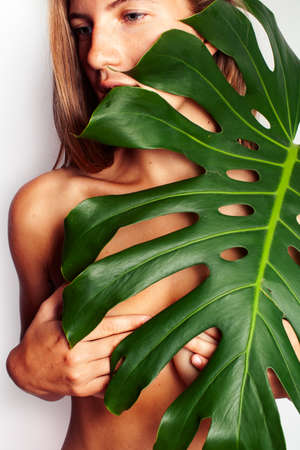 young pretty blond girl naked posing isolated on white background with big green leaf, lifestyle people conceptの写真素材