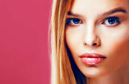young pretty blonde real woman with hairstyle close up and makeup on pink background smilingの写真素材