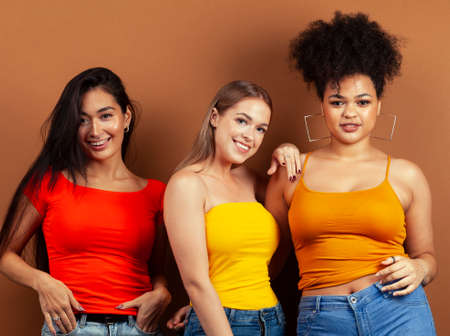 young pretty asian, caucasian, african woman posing cheerful together on brown background, lifestyle diverse nationality people conceptの写真素材