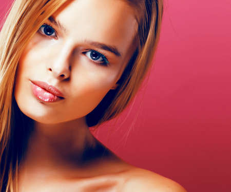 young pretty blonde real woman with hairstyle close up and makeup on pink background smilingの写真素材