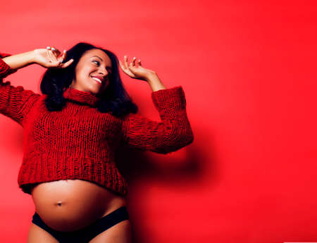 close up portrait of pregnant woman with big belly, hands hold, red sweater on background, choise of gender, lifestyle people conceptの写真素材