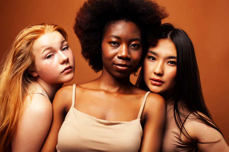 young pretty caucasian, african, scandinavian woman posing cheerful together on brown background, lifestyle diverse nationality people conceptの写真素材