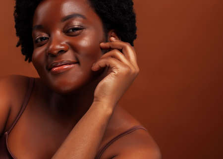 pretty young african american woman with curly hair posing cheerful gesturing on brown background, lifestyle people conceptの写真素材