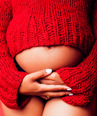 close up portrait of pregnant woman with big belly, hands hold, red sweater on background, choise of gender, lifestyle people conceptの写真素材