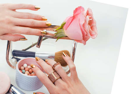 woman hands with golden manicure and many rings holding brushes, cosmetic and rose flower on white background, spa treatment conceptの写真素材