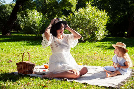 young pretty pregnant brunette woman having fun with her daughter on picnic on green grass in park, lifestyle people conceptの写真素材