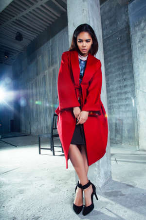 young pretty african american woman in luxury red coat posing fashionable on empty parking building, lifestyle rich people conceptの写真素材