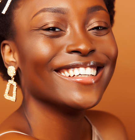 pretty young african american woman with curly hair posing cheerful gesturing on brown background, lifestyle people conceptの写真素材