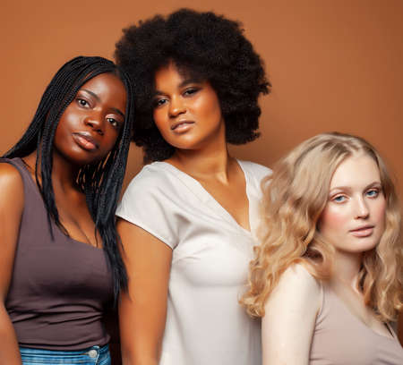 young pretty african and caucasian women posing cheerful together on brown background, lifestyle diverse nationality people conceptの写真素材