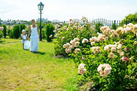 young pretty woman with cute daughter in rose garden at summer happy smiling, lifestyle people conceptの写真素材