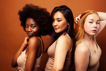 young pretty caucasian, african, scandinavian woman posing cheerful together on brown background, lifestyle diverse nationality people conceptの写真素材