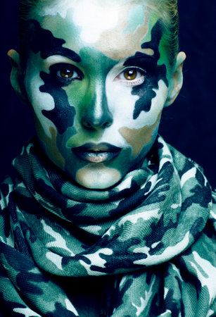 Beautiful young fashion woman with military style clothing and face paint make-up, khaki colors, halloween celebration close up, green patternの写真素材