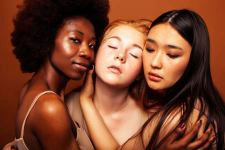 young pretty caucasian, african, scandinavian woman posing cheerful together on brown background, lifestyle diverse nationality people conceptの写真素材
