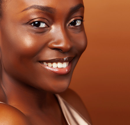 pretty young african american woman with curly hair posing cheerful gesturing on brown background, lifestyle people conceptの写真素材