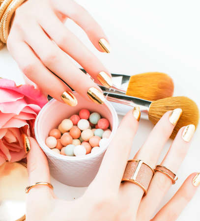woman hands with golden manicure and many rings holding brushes, cosmetic and rose flower on white background, spa treatment conceptの写真素材