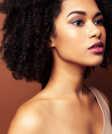 pretty young african american woman with curly hair posing cheerful gesturing on brown background, lifestyle people conceptの写真素材