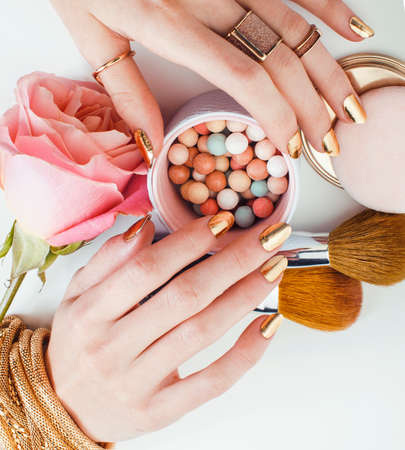 woman hands with golden manicure and many rings holding brushes, cosmetic and rose flower on white background, spa treatment conceptの写真素材