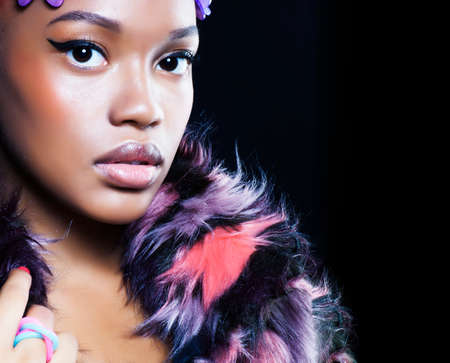 young pretty african american woman in spotted fur coat and flowers on head smiling on black background, fashion people conceptの写真素材