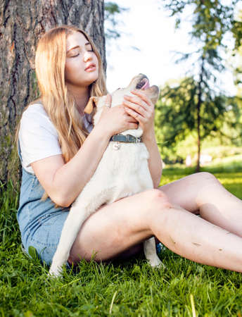 young attractive blond woman playing with her dog in green park at summer, lifestyle people concept, true friendshipの写真素材