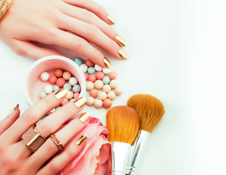 woman hands with golden manicure and many rings holding brushes, cosmetic and rose flower on white background, spa treatment conceptの写真素材