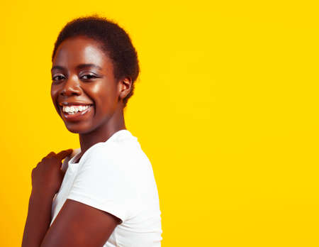 pretty young african american woman with curly hair posing cheerful gesturing on yellow background, lifestyle people conceptの写真素材