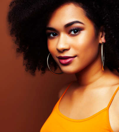 pretty young african american woman with curly hair posing cheerful gesturing on brown background, lifestyle people conceptの写真素材