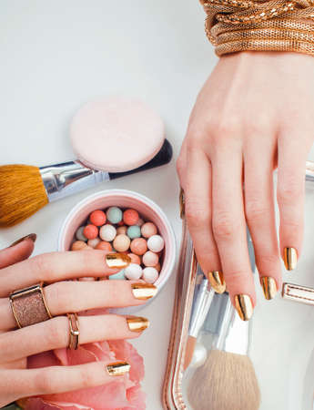 woman hands with golden manicure and many rings holding brushes, cosmetic and rose flower on white background, spa treatment conceptの写真素材