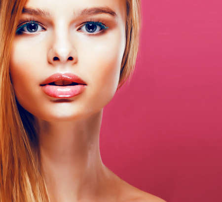 young pretty blonde real woman with hairstyle close up and makeup on pink background smilingの写真素材