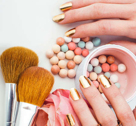 woman hands with golden manicure and many rings holding brushes, cosmetic and rose flower on white background, spa treatment conceptの写真素材