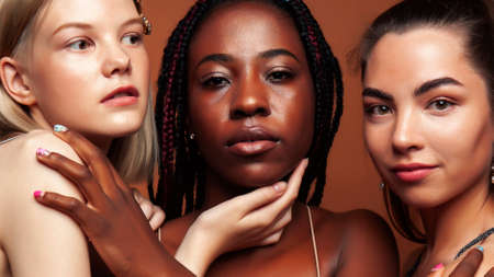 young pretty african and caucasian women posing cheerful together on brown background, lifestyle diverse nationality people conceptの写真素材