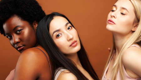 young pretty african and caucasian women posing cheerful together on brown background, lifestyle diverse nationality people conceptの写真素材