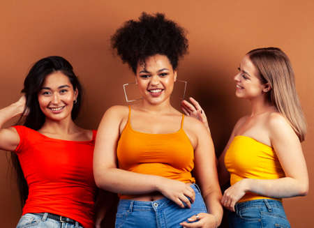 young pretty african and caucasian women posing cheerful together on brown background, lifestyle diverse nationality people conceptの写真素材