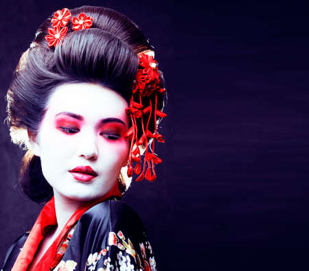 young pretty real geisha in kimono with sakura and decoration on black backgroundの写真素材
