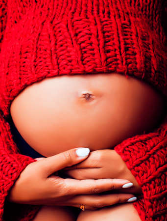 close up portrait of pregnant woman with big belly, hands hold, red sweater on background, choise of gender, lifestyle people conceptの写真素材
