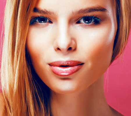 young pretty blonde real woman with hairstyle close up and makeup on pink background smilingの写真素材