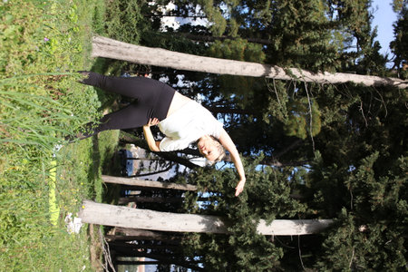 an adult woman doing stretching exercises outside in green parkの写真素材