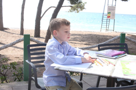 little cute boy with workbook doing homework on table outside in cafe, lifestyle people conceptの写真素材
