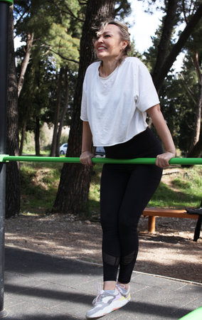 an adult woman doing stretching exercises outside in green park, mental setting training